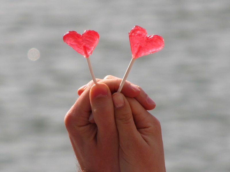 2 red love heart lollipop being held by two clasped hands