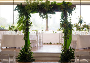 Timber arbour covered with greenery in front of white wedding tables