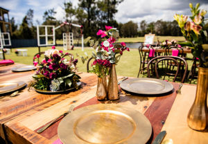 Timber table with gold charger plates and Burgundy flowers in gold vases