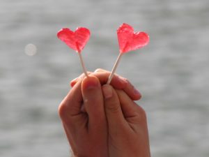 2 red love heart lollipop being held by two clasped hands